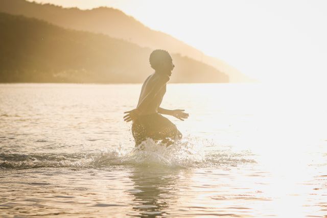 This visually captivating scene features a man joyfully swimming in a tranquil lake at sunset. Ideal for promotions of outdoor recreation, travel destinations, wellness retreats, and summer adventure activities. The serene nature background suggests relaxation and harmony with nature.
