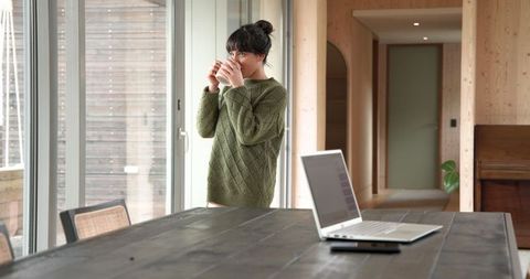 Woman Relaxing by Glass Door with Coffee in Modern Home