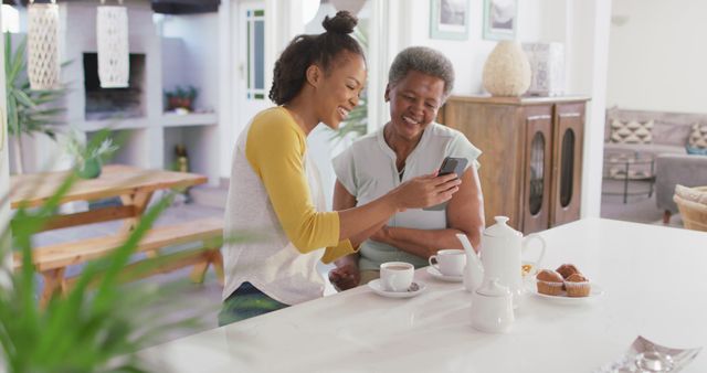 Smiling Grandmother and Granddaughter Looking at Smartphone at Kitchen Table - Download Free Stock Images Pikwizard.com