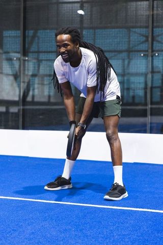 Crouching man gripping padel racket on blue court