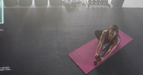Woman stretching on pink mat in gym practicing seated forward bend for flexibility