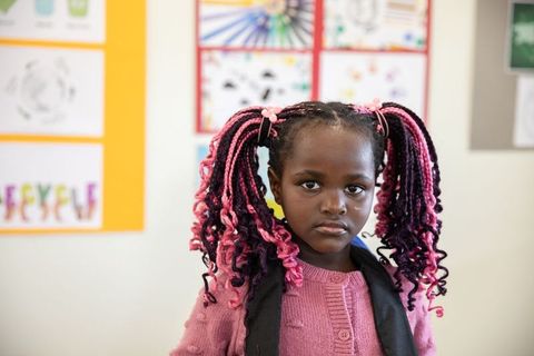 Young girl proudly displays classroom artwork with pink braids