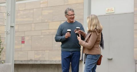 Mature couple sharing takeaway coffee and friendly conversation in urban plaza