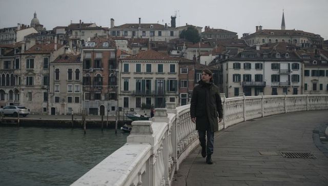 Walking through historic Venetian canal district on stone bridge with overcast sky