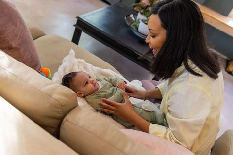 Mother engaging with newborn on sofa blanket, cozy at-home bonding moment
