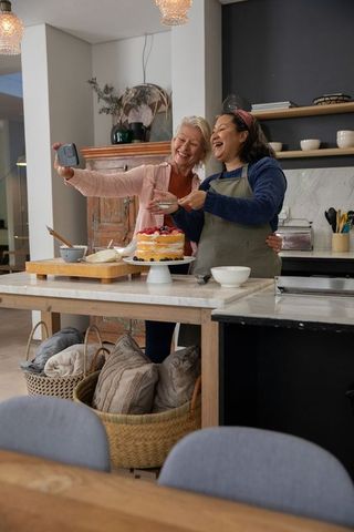 Multigenerational friends taking selfie while decorating berry cake on kitchen island