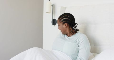 African american woman sitting up in bed touching duvet in serene minimalist bedroom