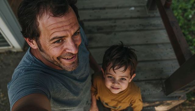 Smiling father and son taking selfie on front porch wooden steps while bonding outdoors