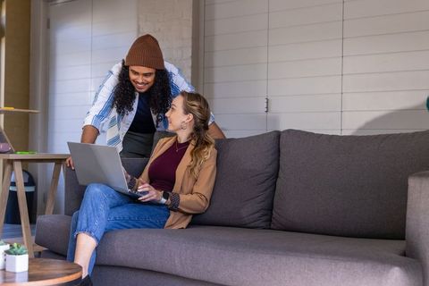Diverse coworkers collaborating on laptop while relaxing on modern gray sofa in lounge