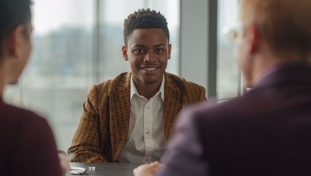 Young professional smiling and making eye contact during panel interview in modern boardroom