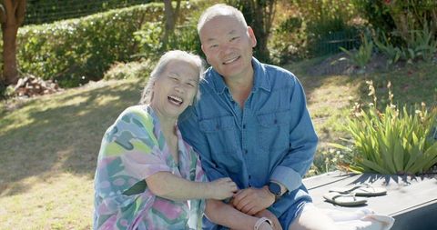 Senior asian couple laughing and embracing in sunlit garden, relaxed outdoor lifestyle