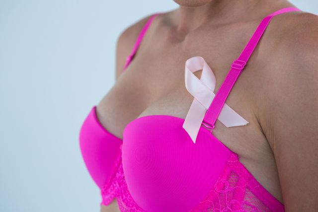 Mid section of woman in pink bra with Breast Cancer Awareness ribbon against gray background