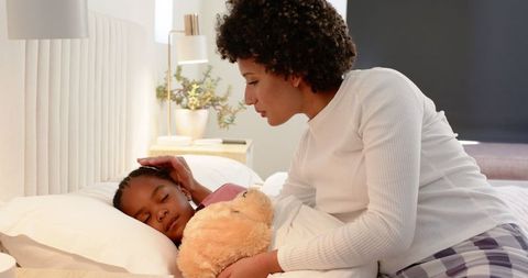Mother caring for sleeping child in bed with teddy bear
