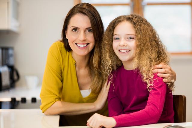 Mother and daughter smiling together in a kitchen, showcasing family bonding and happiness. Ideal for use in family-oriented advertisements, parenting blogs, lifestyle magazines, and home-related content.