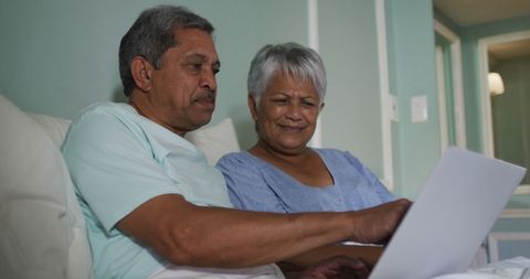 Senior Biracial Couple Enjoying Relaxed Laptop Time in Bed