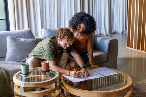 Couple signing documents on glass coffee table in modern living room, planning move