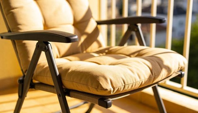 Sunlit beige cushioned patio chair with tufted seat and metal frame on balcony railing for outdoor l