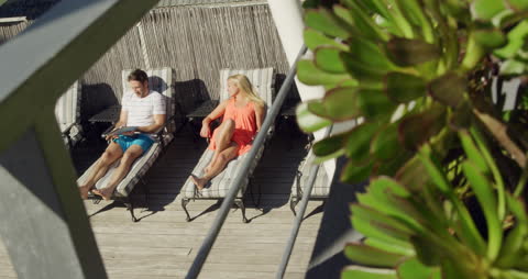 Relaxing Couple Lounging on Balcony Using Laptop