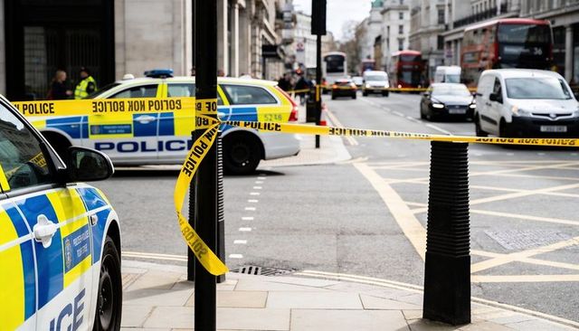 Police cordoning busy city street with yellow tape, patrol cars and officers in hi-vis
