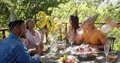 Friends toasting and celebrating 30th birthday on sunny backyard deck with gold balloons
