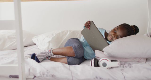 Smiling african american girl using tablet lying on bunk bed at home, copy space. Technology, communication and domestic life.