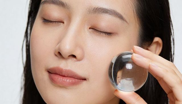 Asian woman holding glass sphere against cheek for skincare beauty and wellness concept