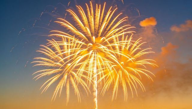 Golden fireworks blooming over dusk sky with drifting smoke and horizon glow