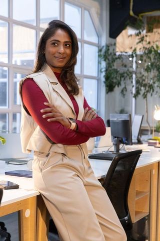 Confident indian businesswoman leaning on desk in modern coworking office wearing smartwatch