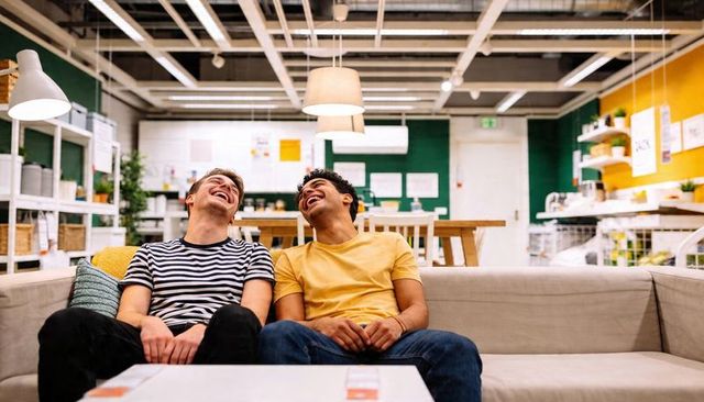 Two friends laughing on sofa in furniture showroom with price tags and modern lighting