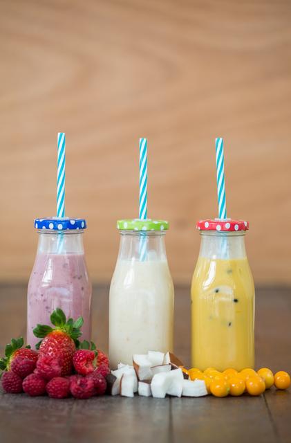 Three bottles with smoothies and fresh chopped fruits on wooden board