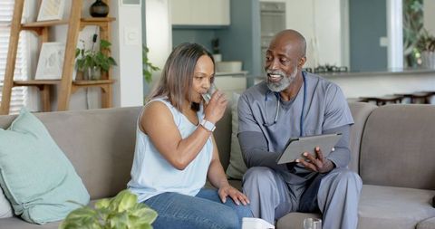 Diverse caregiver consulting with mature woman at home using tablet, reviewing care plan
