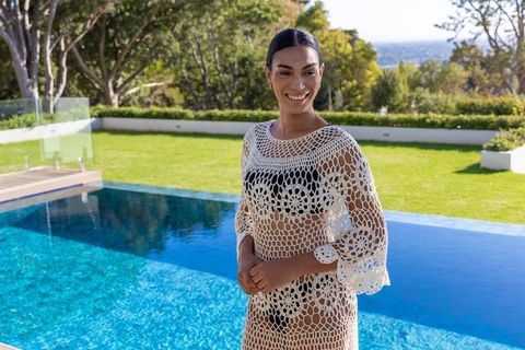 African american woman wearing white crochet coverup over black swimsuit by pool, smiling