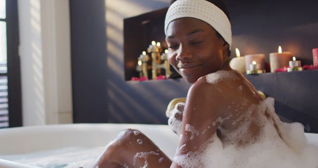 Smiling african american woman with towel taking bath and touching her skin in bathroom. health and beauty concept.