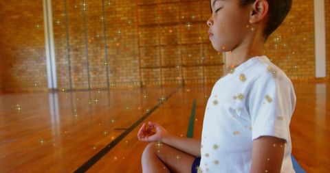 Child meditating on yoga mat in gymnasium with sparkle overlay for mindfulness