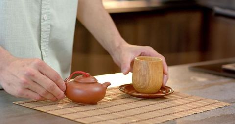 Man Arranging Clay Teapot and Wooden Cup in Rustic Kitchen
