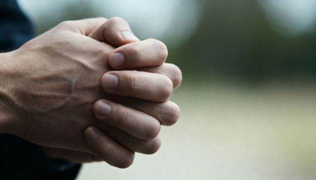 Clasping adult hands closeup showing veins and texture outdoors with blurred green bokeh