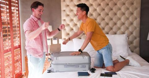 Excited Gay Couple Packing for Vacation on Bed