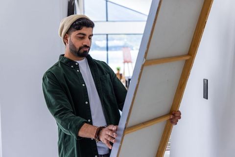 Artist holding large stretched canvas in bright studio preparing to hang modern artwork