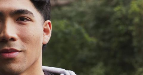 Half-face closeup of young asian man in gray hoodie with green bokeh and copy space