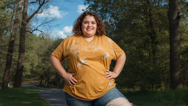 Confident plus-size woman smiling in paint-stained mustard tee on park path