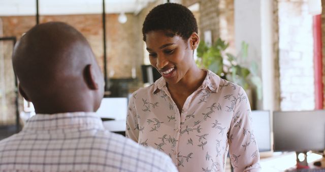 Coworkers engaging in a casual discussion in a stylish, modern office environment. Can be used for images depicting friendly workplace interactions, team collaborations, and positive office culture.