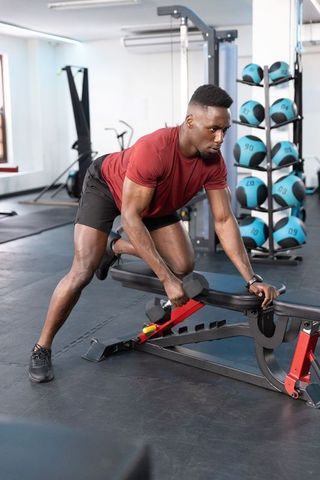African-american man performing one-arm dumbbell row on bench during intense gym workout