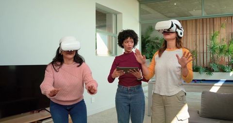Women wearing VR headsets collaborating with tablet in bright living room