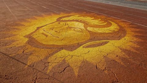 Sun face mural spreading over cracked red running track with bold yellow rays