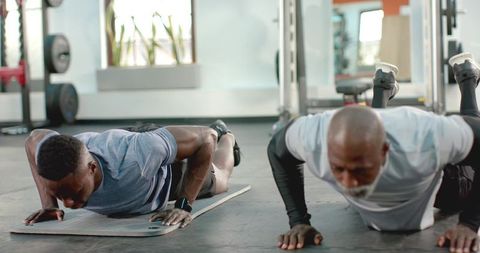 African american adult and senior men doing push-ups together at gym for strength training