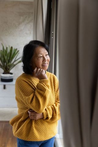 Senior woman in mustard sweater contemplating by window at home