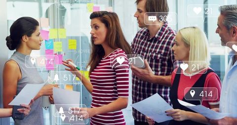 Woman leading creative brainstorming session at glass wall with sticky notes and team