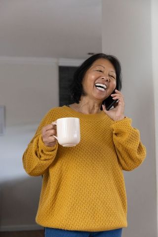 Cheerful senior woman enjoying phone call at home with mug