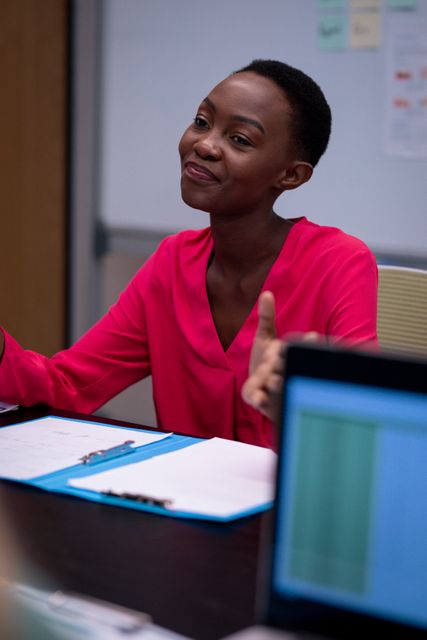 African american businesswoman smiling and gesturing to colleagues in office meeting. working in business at a modern office.