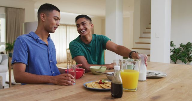 Smiling biracial gay male couple having breakfast together in kitchen. staying at home in isolation during quarantine lockdown.